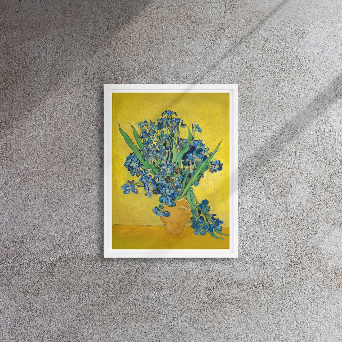 Van Gogh's 'Vase with Irises Against a Yellow Background' on a 12"x16" white framed canvas print on a textured gray wall.
