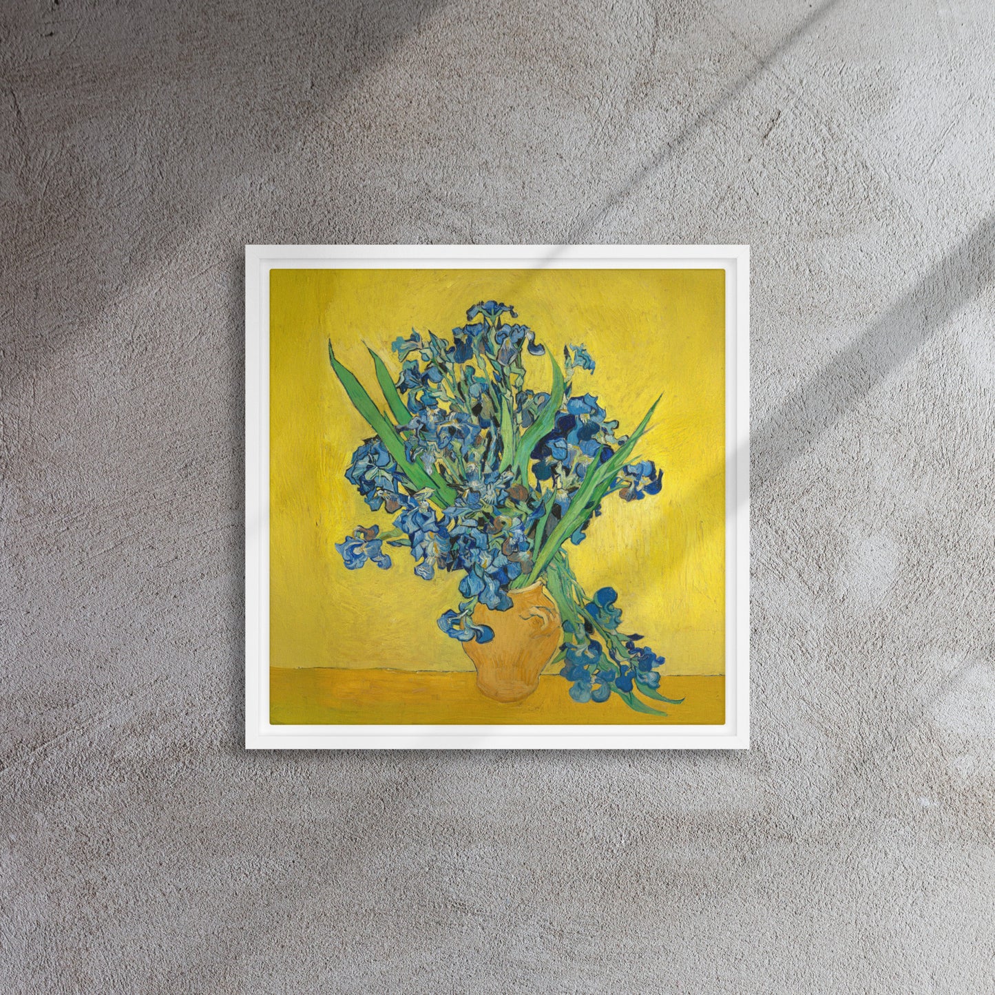 Van Gogh's 'Vase with Irises Against a Yellow Background' on a 16"x16" white framed canvas print on a textured gray wall.