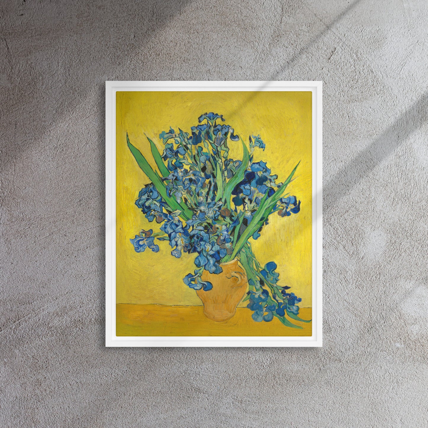 Van Gogh's 'Vase with Irises Against a Yellow Background' on a 16"x20" white framed canvas print on a textured gray wall.