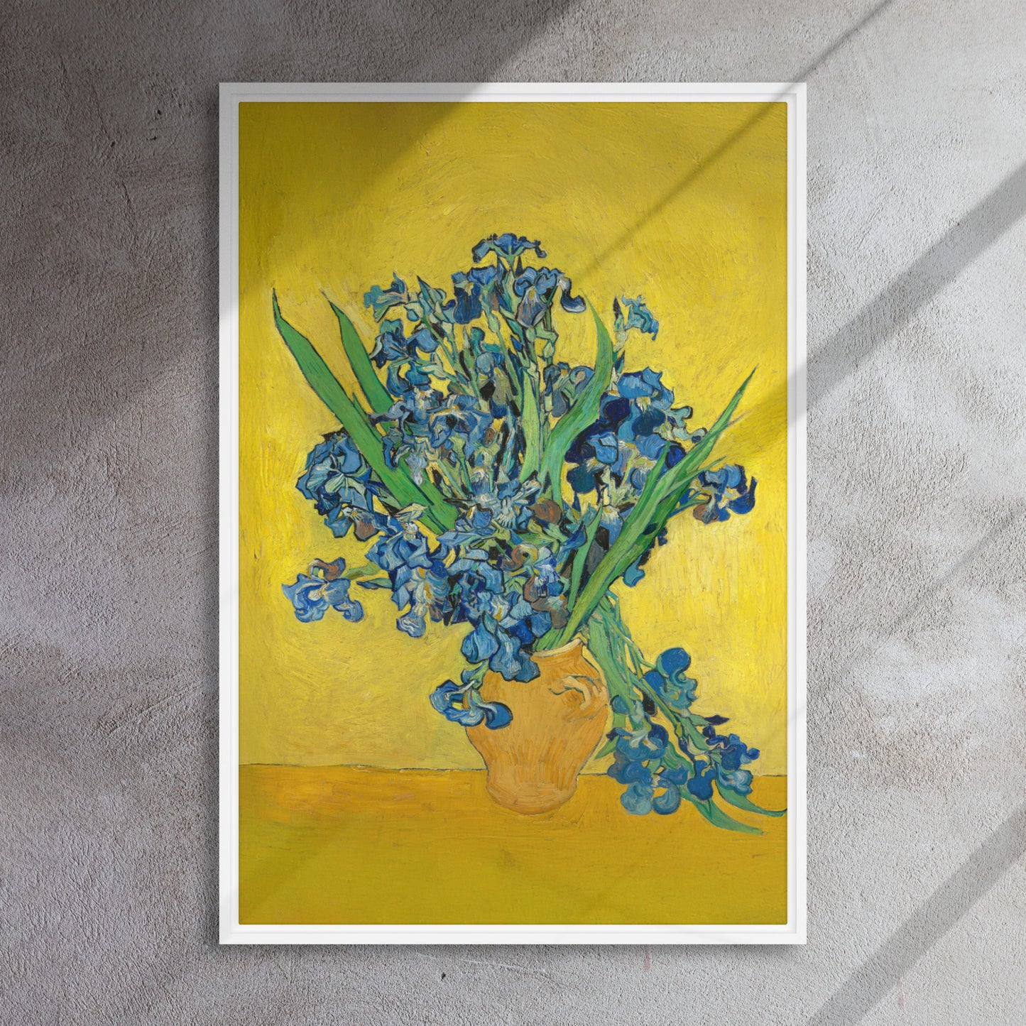 Van Gogh's 'Vase with Irises Against a Yellow Background' on a 24"x36" white framed canvas print on a textured gray wall.