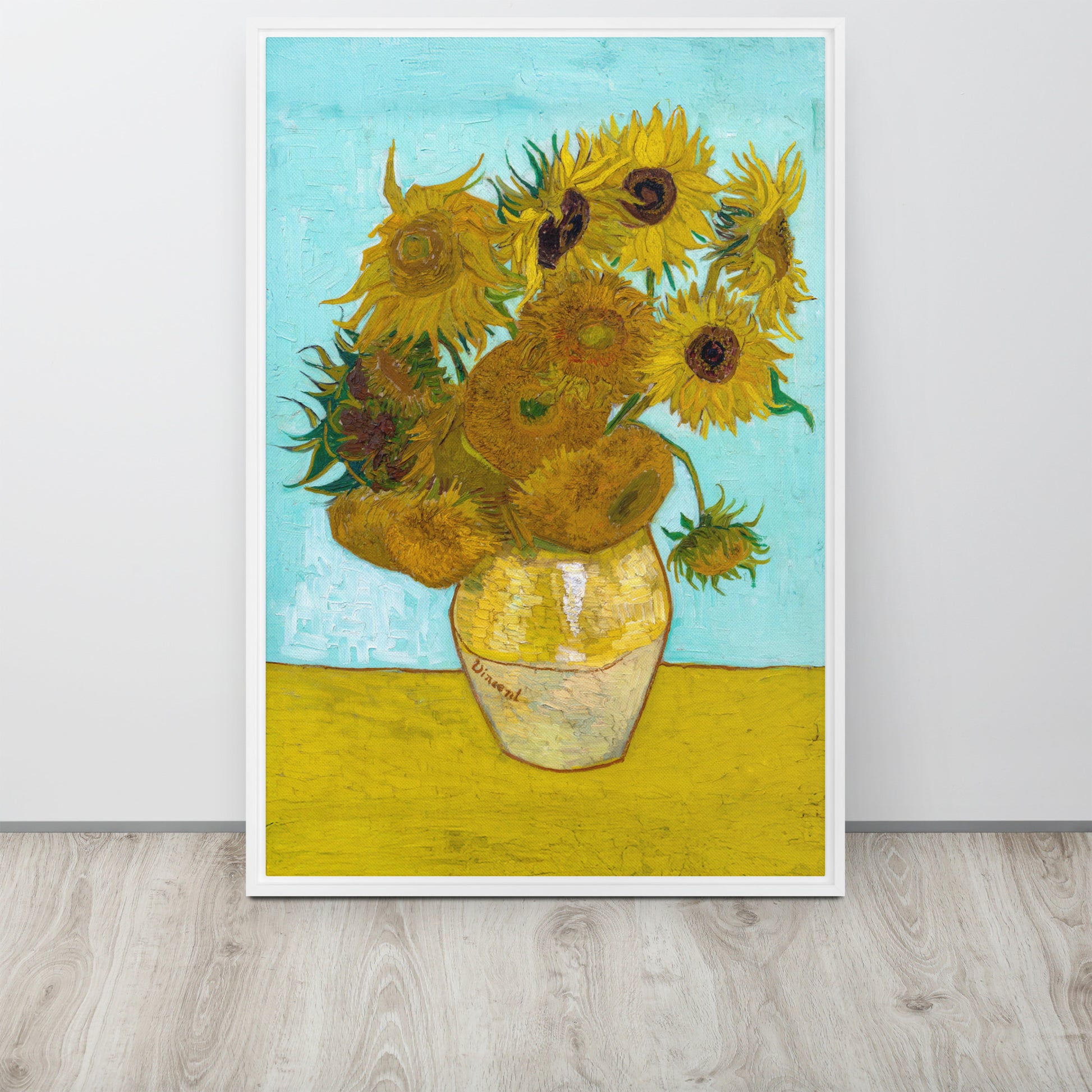 Van Gogh's 'Vase with Twelve Sunflowers' on a 24"x36" white framed canvas print sitting on a wooden floor leaning against a light gray wall.