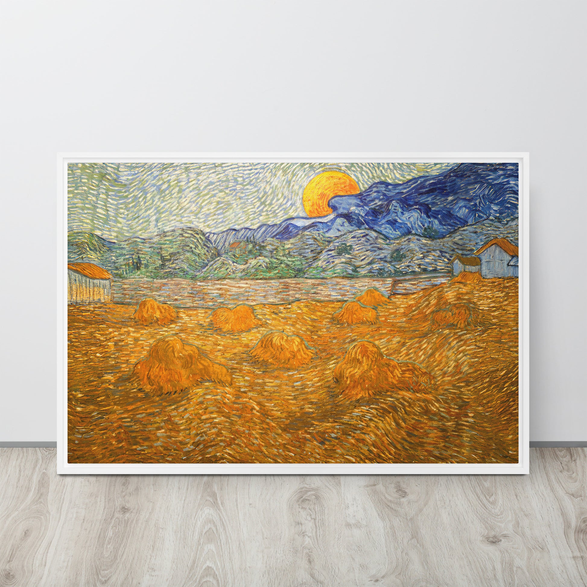 Van Gogh's 'Landscape with Wheat Sheaves and Rising Moon' on a 24"x36" white framed canvas print sitting on a wooden floor leaning against a light gray wall.