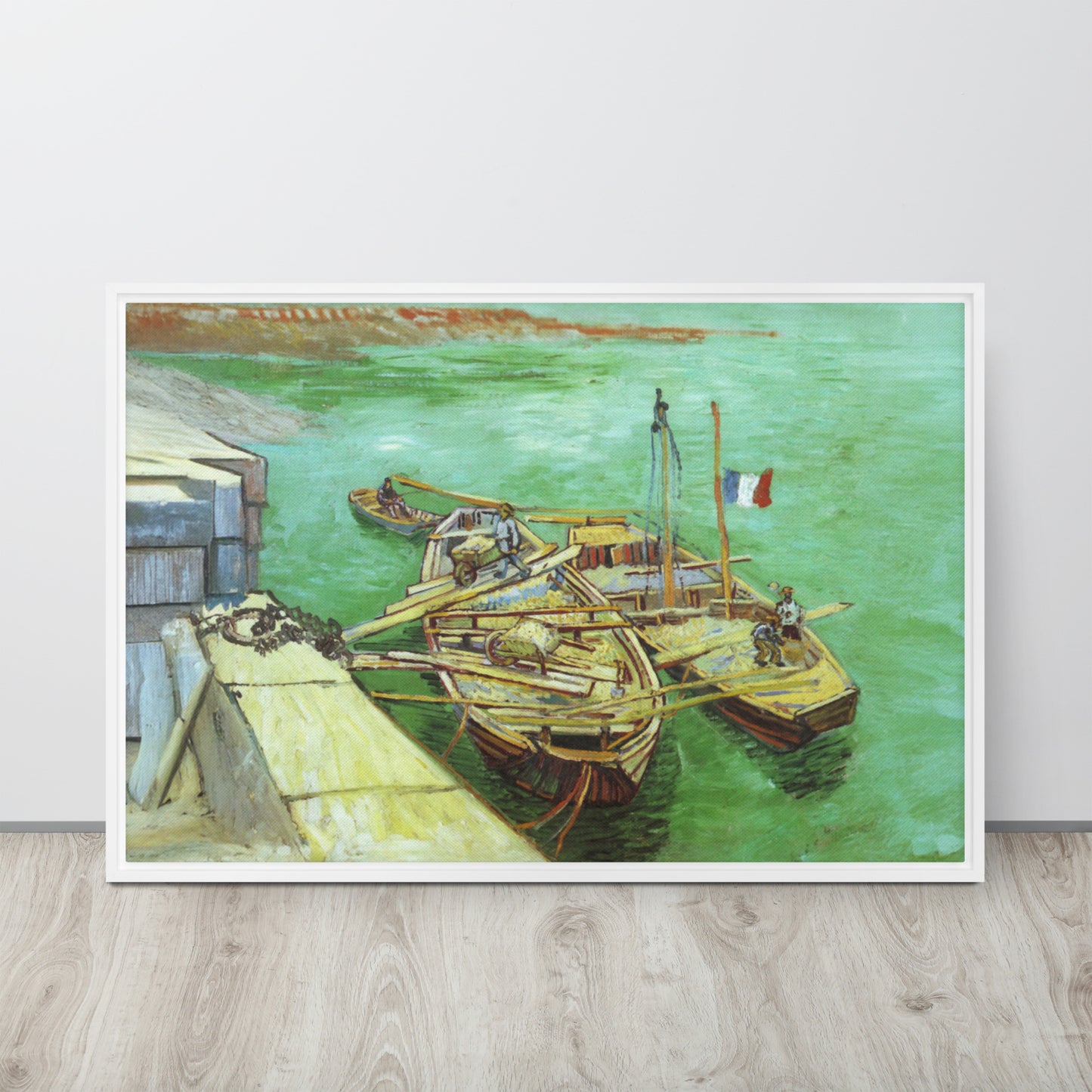 Van Gogh's 'Quay with Men Unloading Sand Barges' on a 24"x36" white framed canvas print sitting on a wooden floor leaning against a light gray wall.