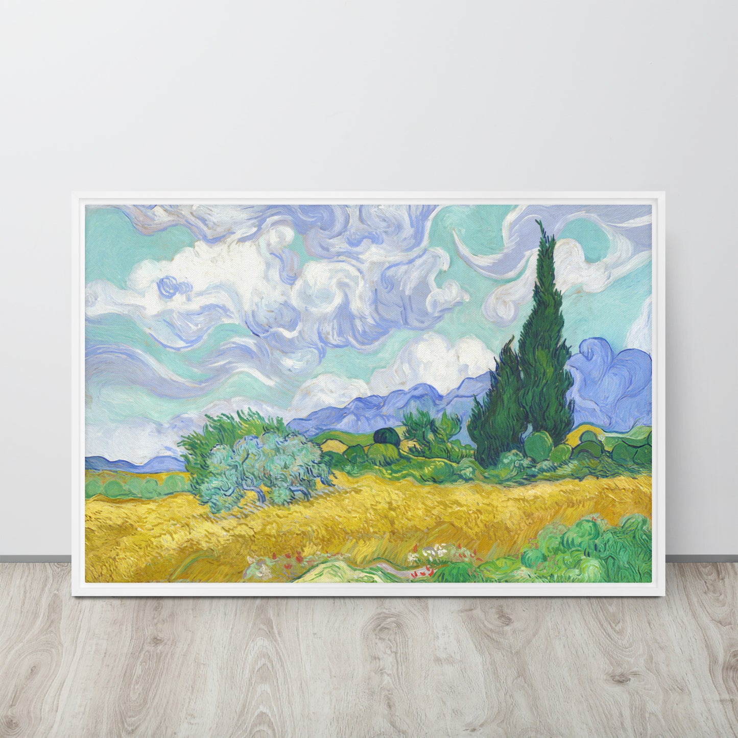 Van Gogh's 'Wheat Field with Cypresses' on a 24"x36" white framed canvas print sitting on a wooden floor leaning against a light gray wall.
