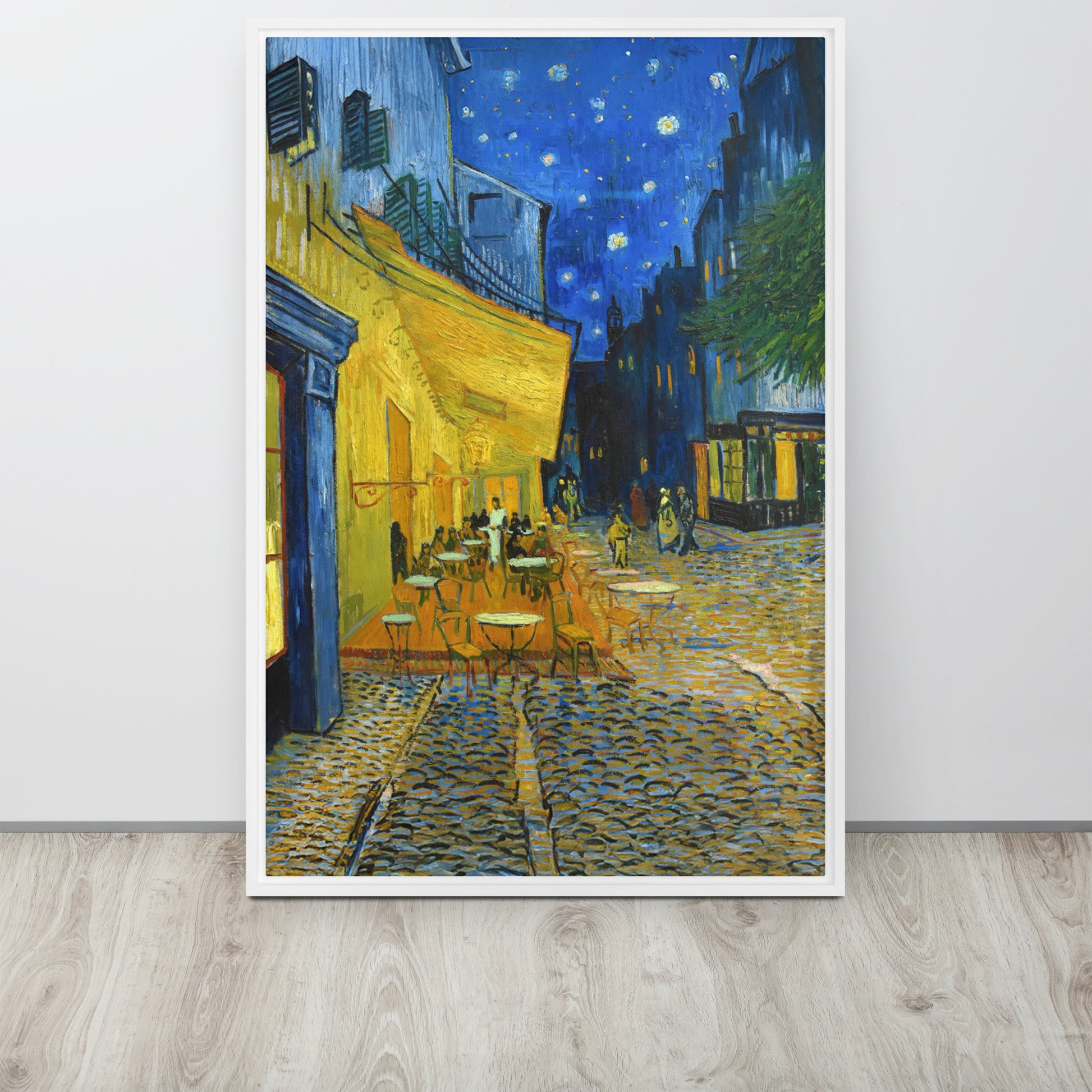 Van Gogh's 'Café Terrace at Night' on a 24"x36" white framed canvas print sitting on a wooden floor leaning against a light gray wall.