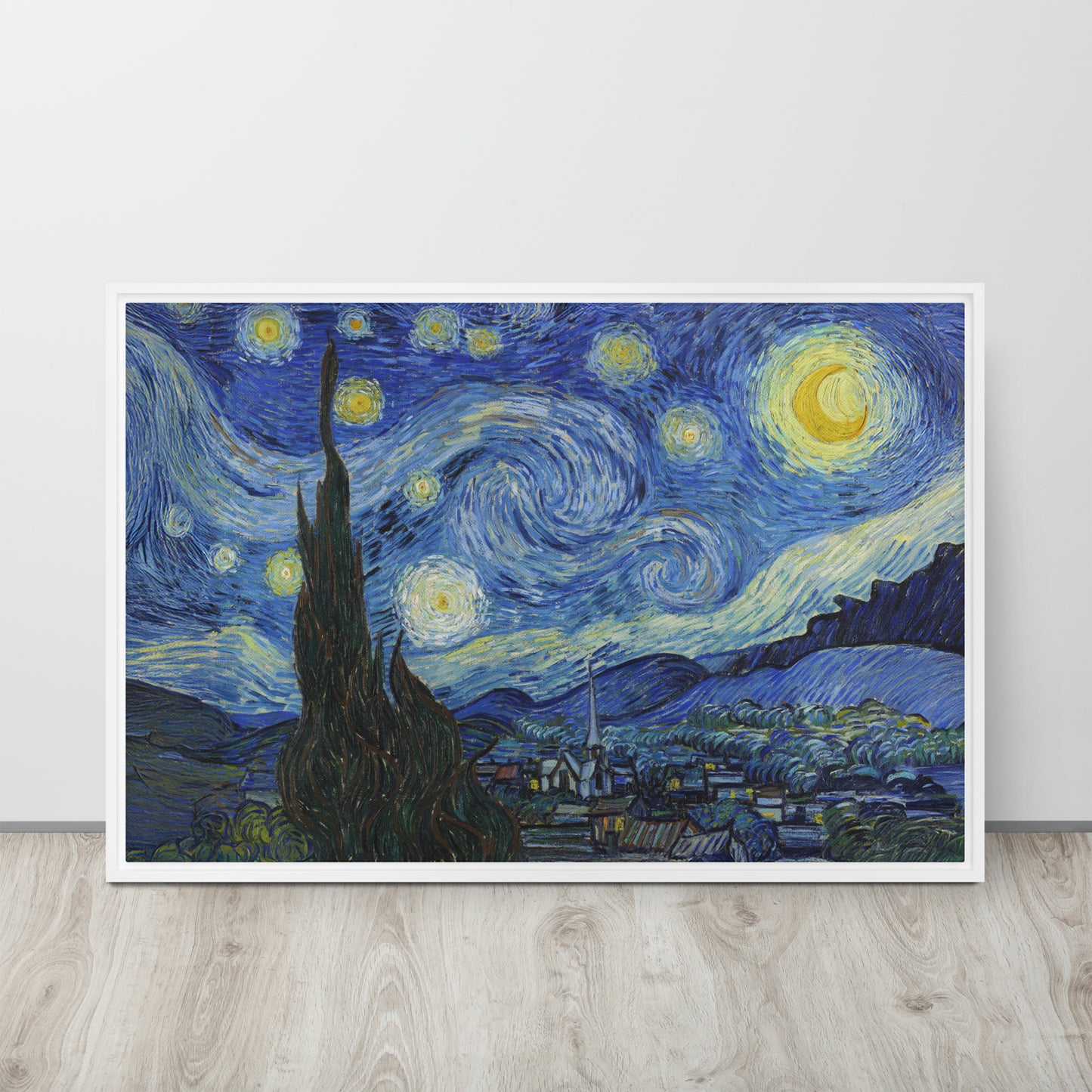 Van Gogh's 'Starry Night' on a 24"x36" white framed canvas print sitting on a wooden floor leaning against a light gray wall.